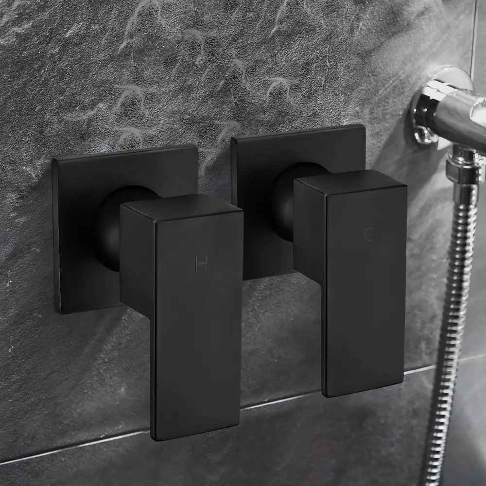 Wall-mounted matte black shower mixer valve handles with hot and cold indicators installed on modern grey tiled bathroom wall