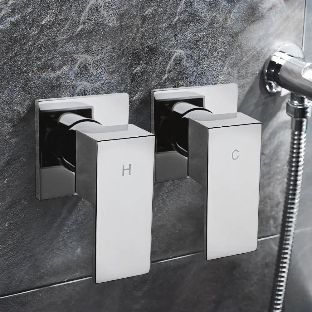 Wall-mounted chrome shower mixer valve handles with hot and cold indicators installed on modern grey tiled bathroom wall