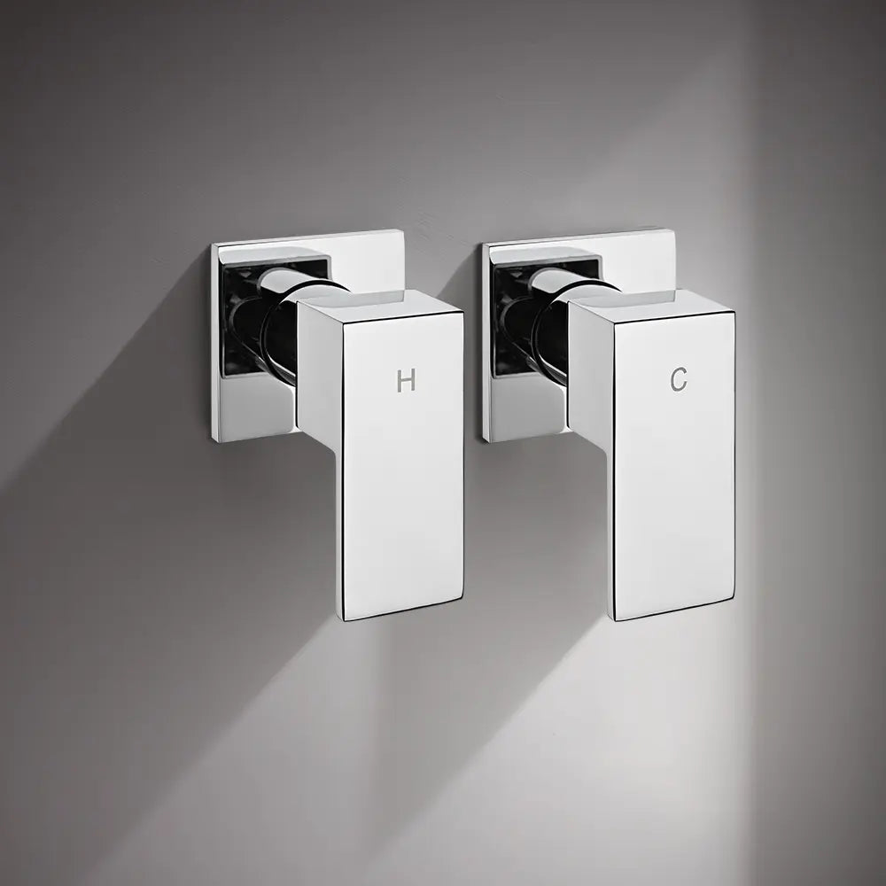 Wall-mounted chrome shower mixer valve handles with hot and cold indicators installed on grey bathroom wall