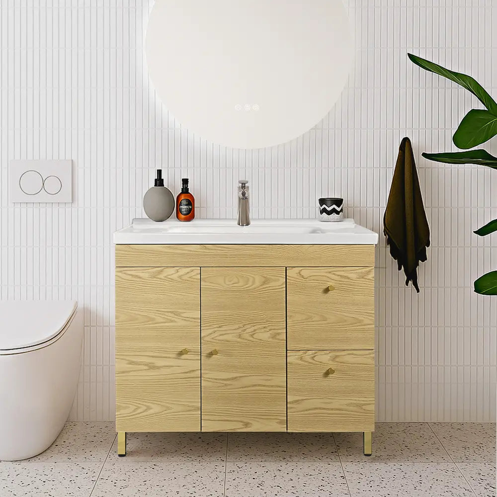 Light oak bathroom vanity with white ceramic basin and gold handles. 