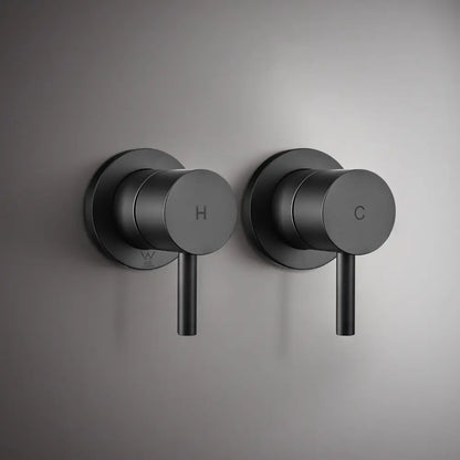 Wall-mounted black round shower mixer valve handles with hot and cold indicators on modern grey bathroom wall
